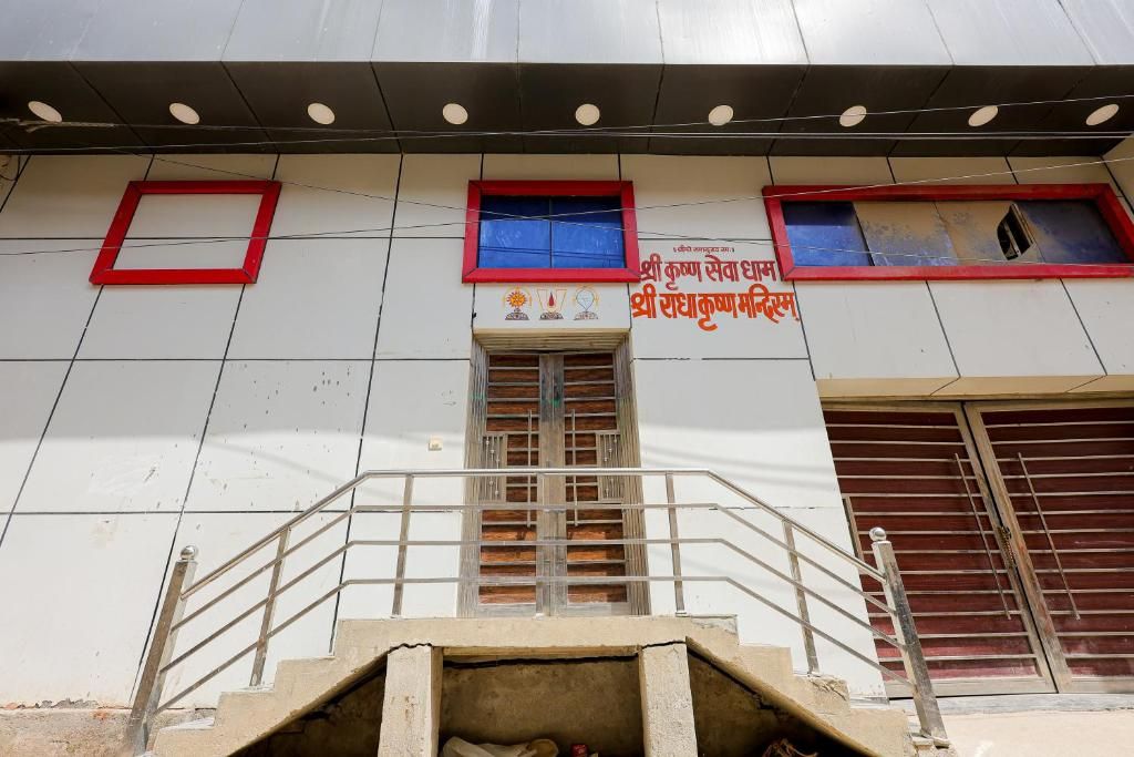 A building with a staircase leading to a door, a window with a red frame, and a sign with text.