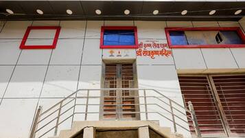 A building with a staircase leading to a door, a window with a red frame, and a sign with text.