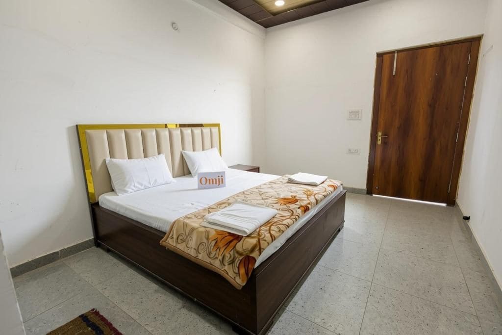 A single bed with a headboard, a bedside table, a wooden wardrobe, and a sign with the name 'Omji' on the wall.
