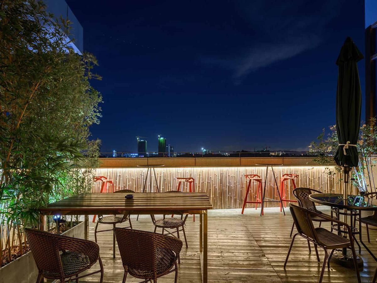 Eine Terrasse im Freien mit einem Holztisch und -stühlen, einem Bambuszaun und einer Stadtansicht im Hintergrund.