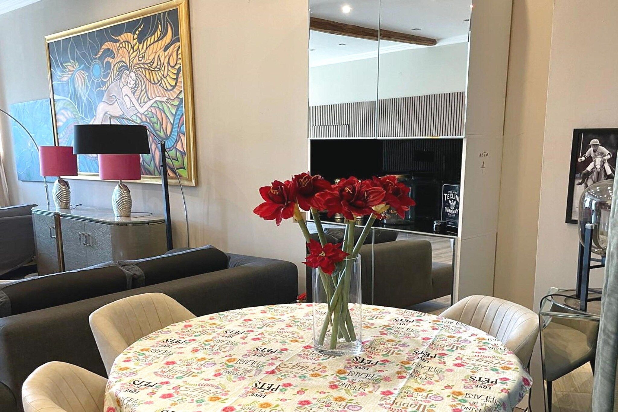 Ein modernes Wohnzimmer mit einem runden Tisch, Sofas, einem Gemälde und einer Vase mit roten Blumen.