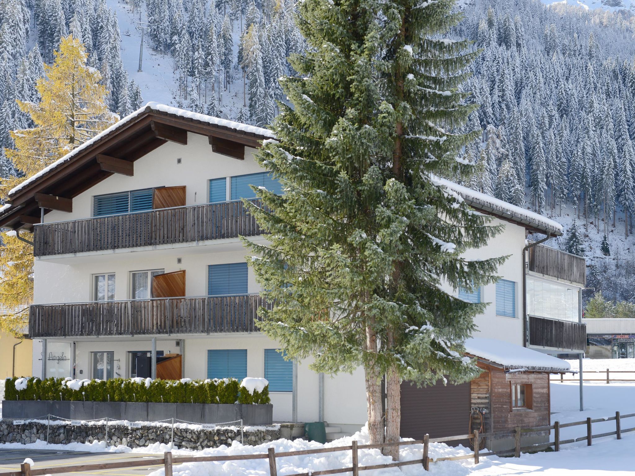 A multi-story building with balconies, a stone wall, and a snow-covered mountain backdrop.