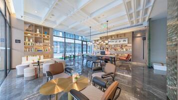 A spacious lobby with a central seating area, a large bookshelf, and a view through the glass wall.