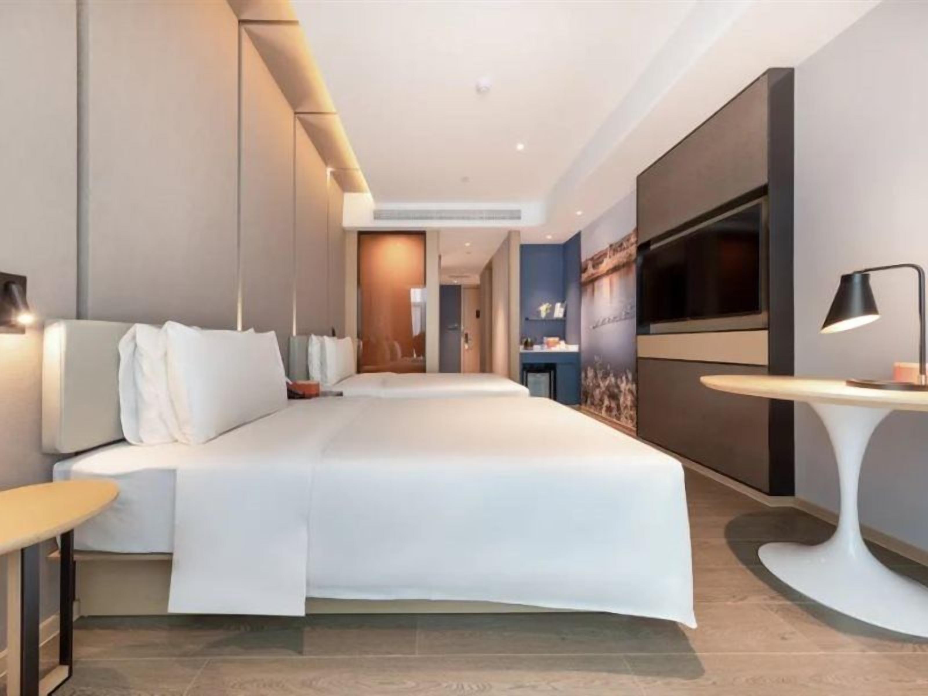 A modern hotel room with a large bed, a flat-screen TV, a desk, and a seating area.