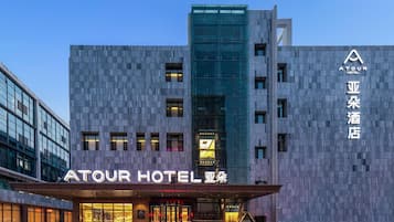 A modern hotel with a prominent glass facade, a well-lit entrance, and signage indicating it is the Atour Hotel.