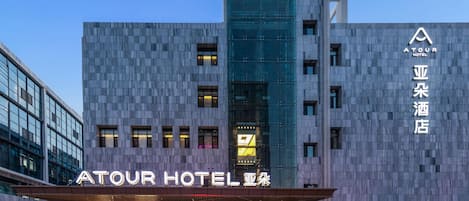 Ett modernt hotell med en framträdande fasad av glas, en väl upplyst entré och skyltar som visar att det är Atour Hotel.