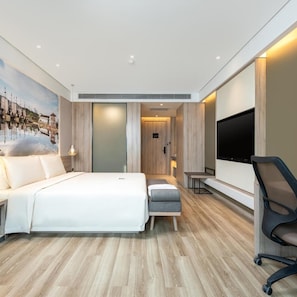 A modern hotel room with a large bed, a flat-screen TV, and a wooden floor.