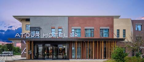 A modern hotel with a prominent entrance, a glass facade, and a sign indicating it's the ATOUR HOTEL.