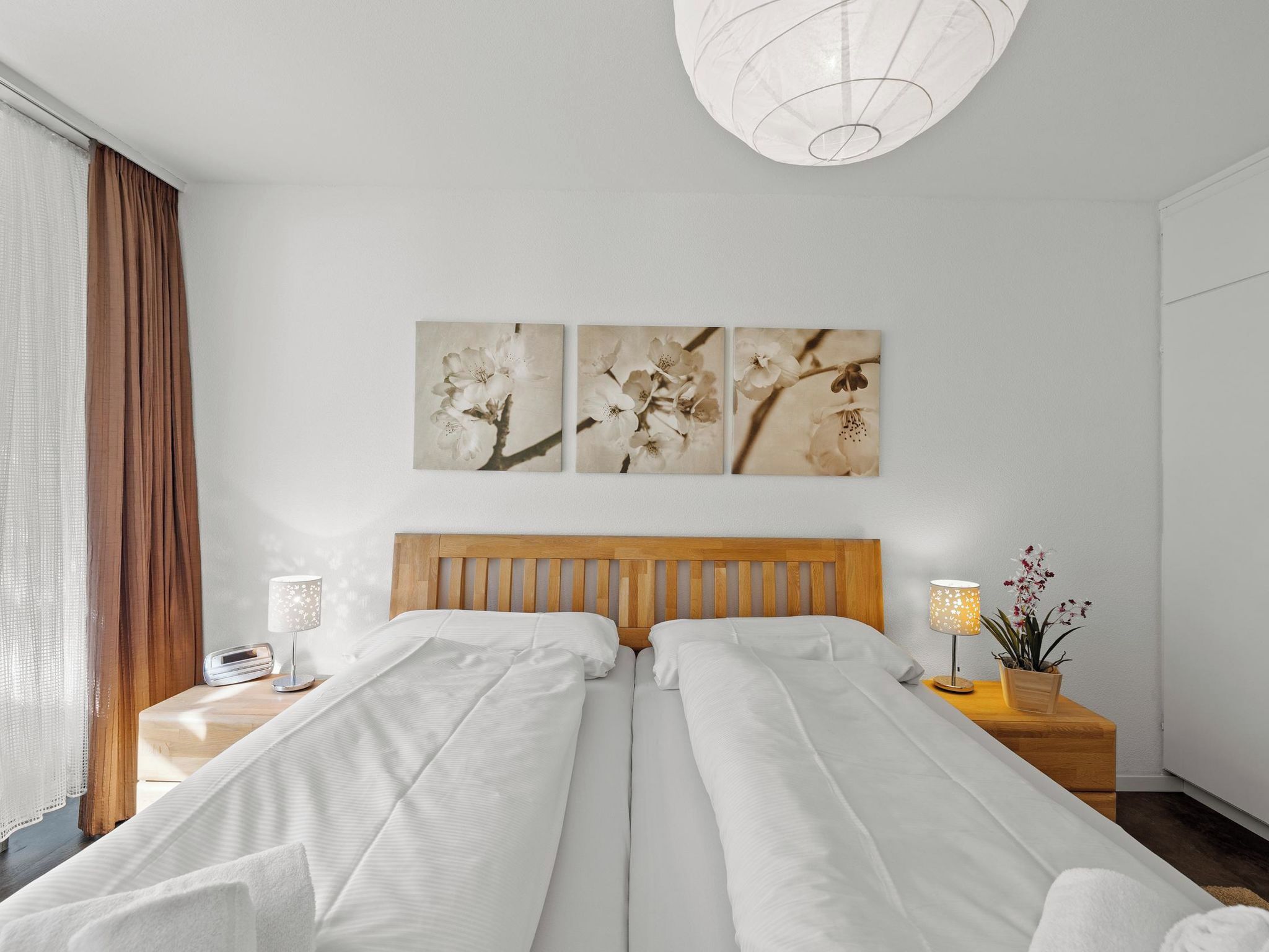 Ein Hotelzimmer mit zwei Betten, einem Holzkopfteil, einem Nachttisch mit Lampe und einem an der Wand befestigten Blumenbild.