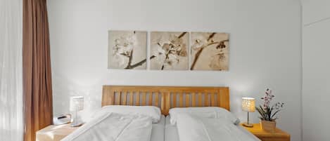 A hotel room with two beds, a wooden headboard, a nightstand with a lamp, and a wall-mounted artwork of flowers.