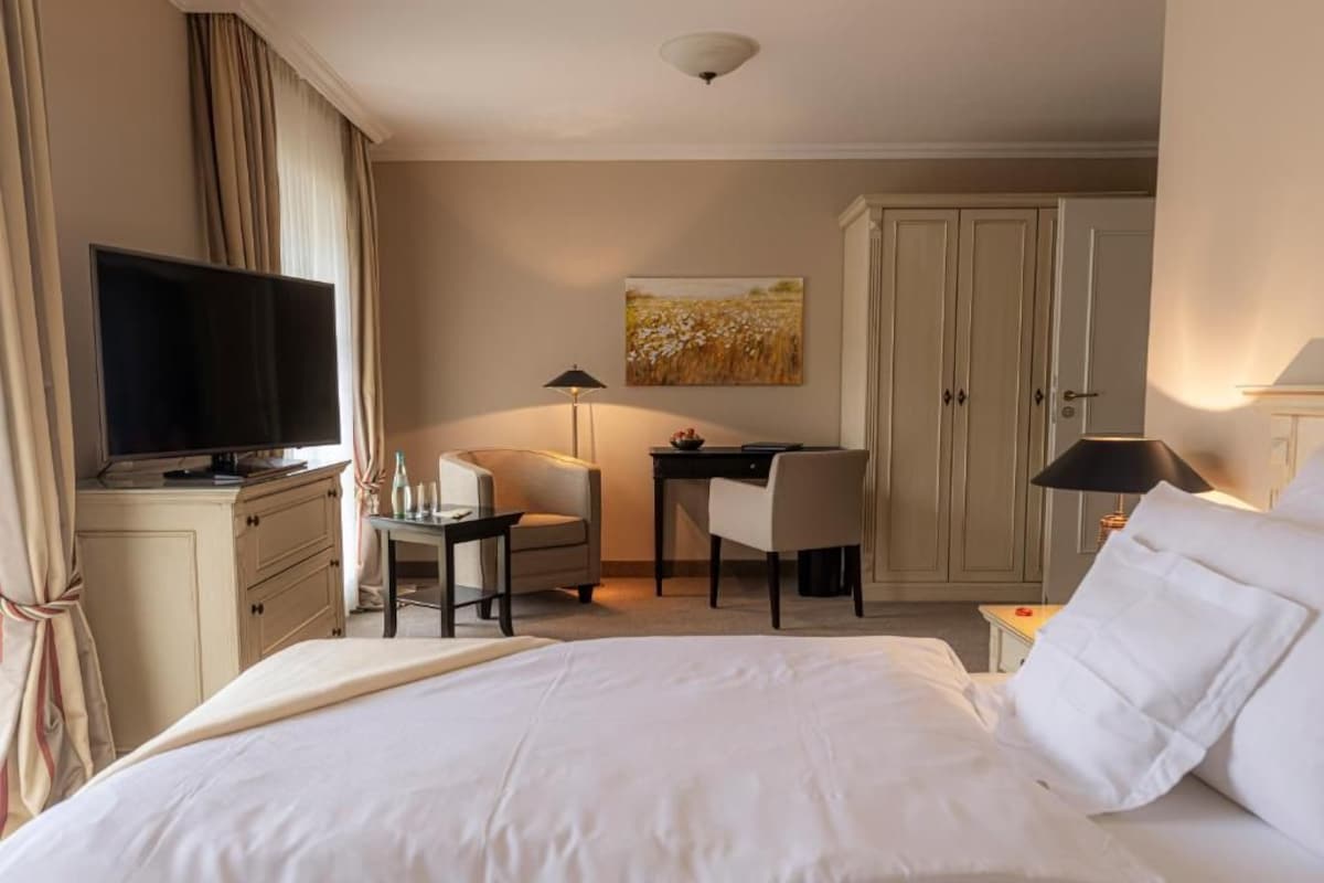 A hotel room with a bed, a desk, a chair, a television, and a wardrobe.