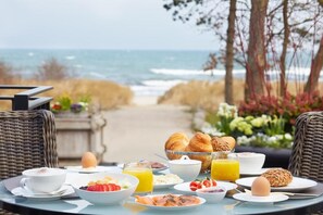 A breakfast table with croissants, eggs, and fruit, overlooking the ocean. - Strandhotel Fontana (Timmendorfer Strand)
