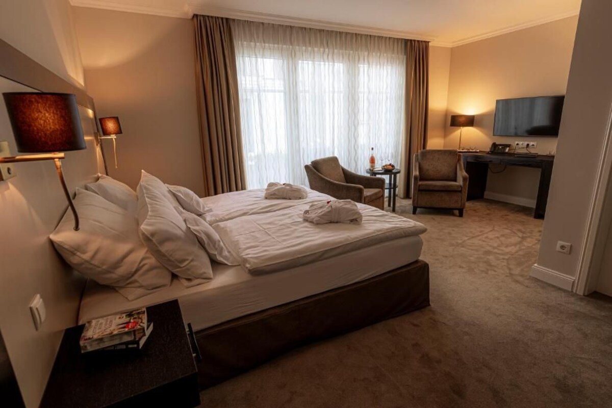 A hotel room with a large bed, a desk, a chair, a television, and a window with curtains.
