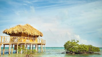 Una cabaña de madera sobre el agua con techo de paja, rodeada de aguas cristalinas y una isla de manglares.
