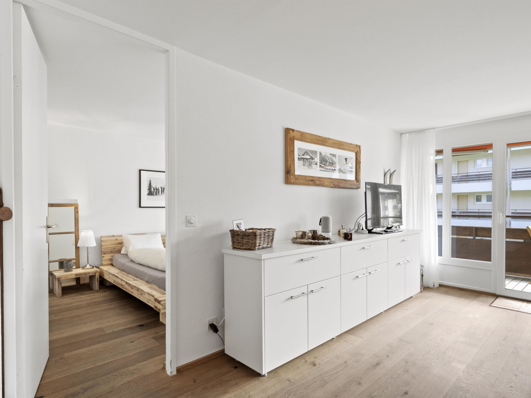 Un dormitorio moderno con cama, mesita de noche, lámpara y un armario blanco con televisor.