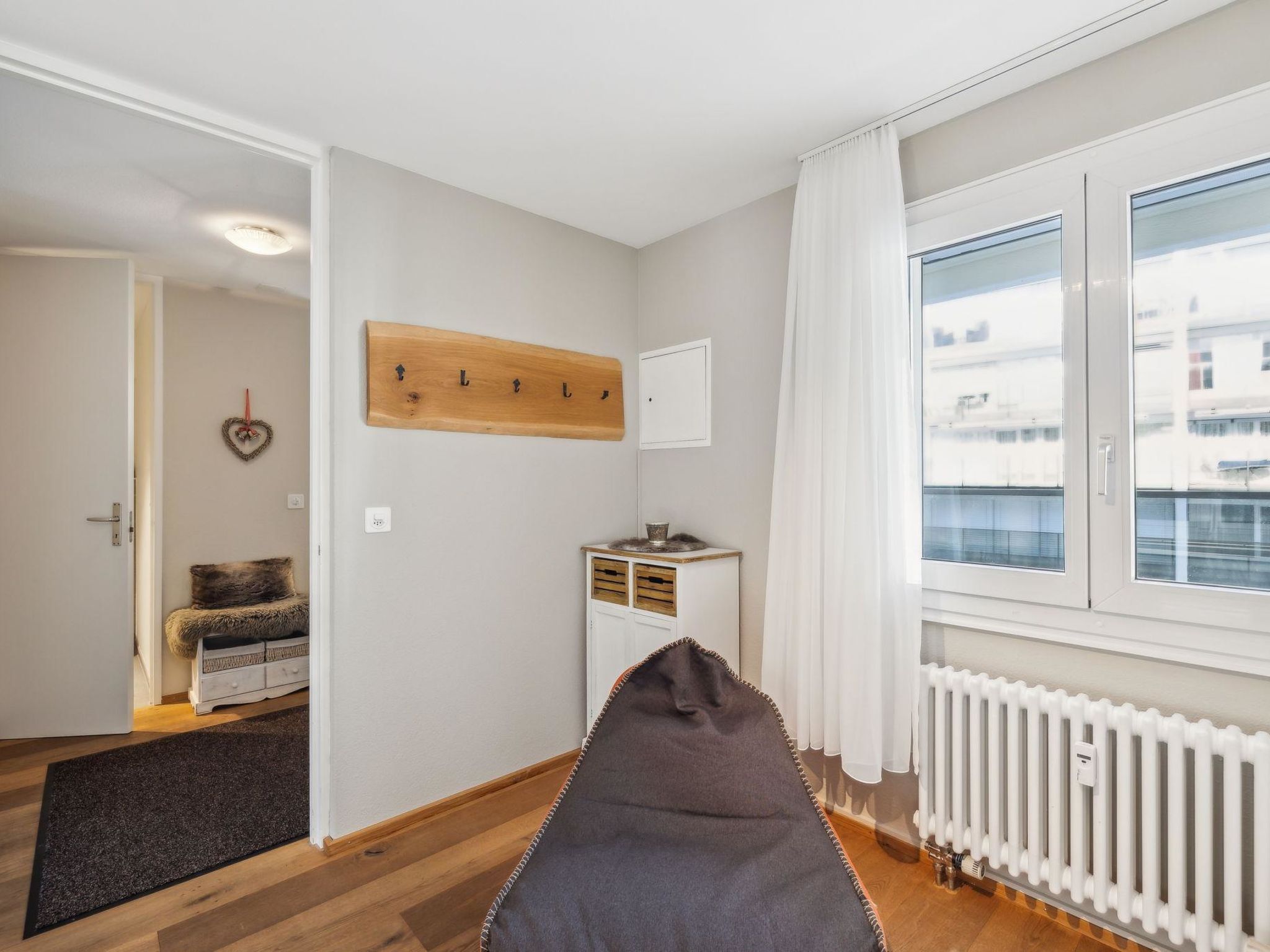 Een kamer met een bed, een radiator, een raam en een deur naar een andere kamer.