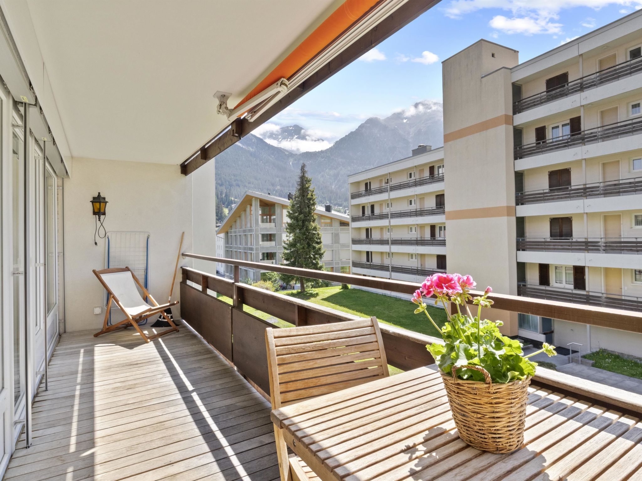 Un balcon avec une table en bois, une chaise et un pot de fleurs.