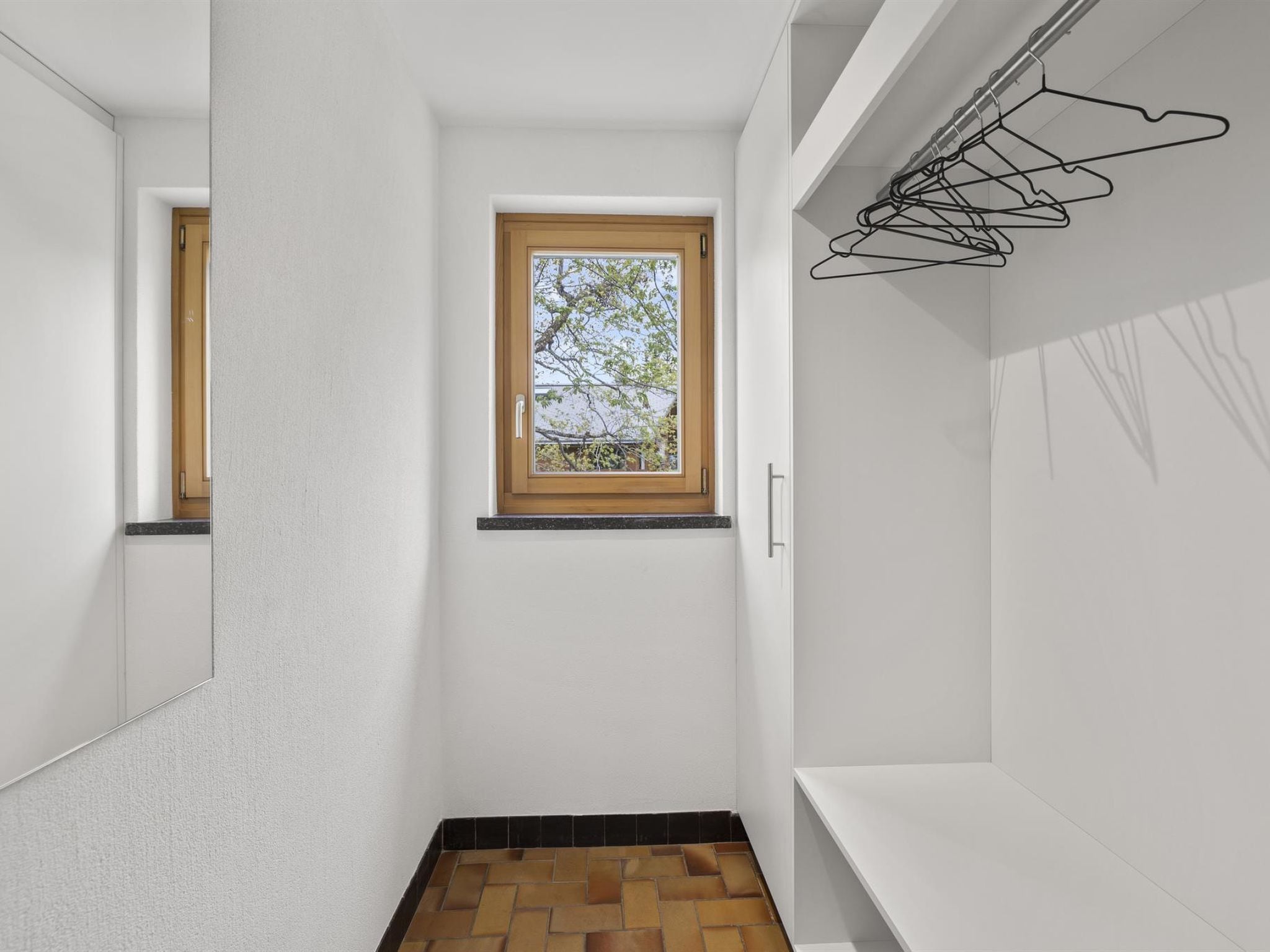 A narrow hallway with a small window, a wooden door, and a wall-mounted clothes rack.