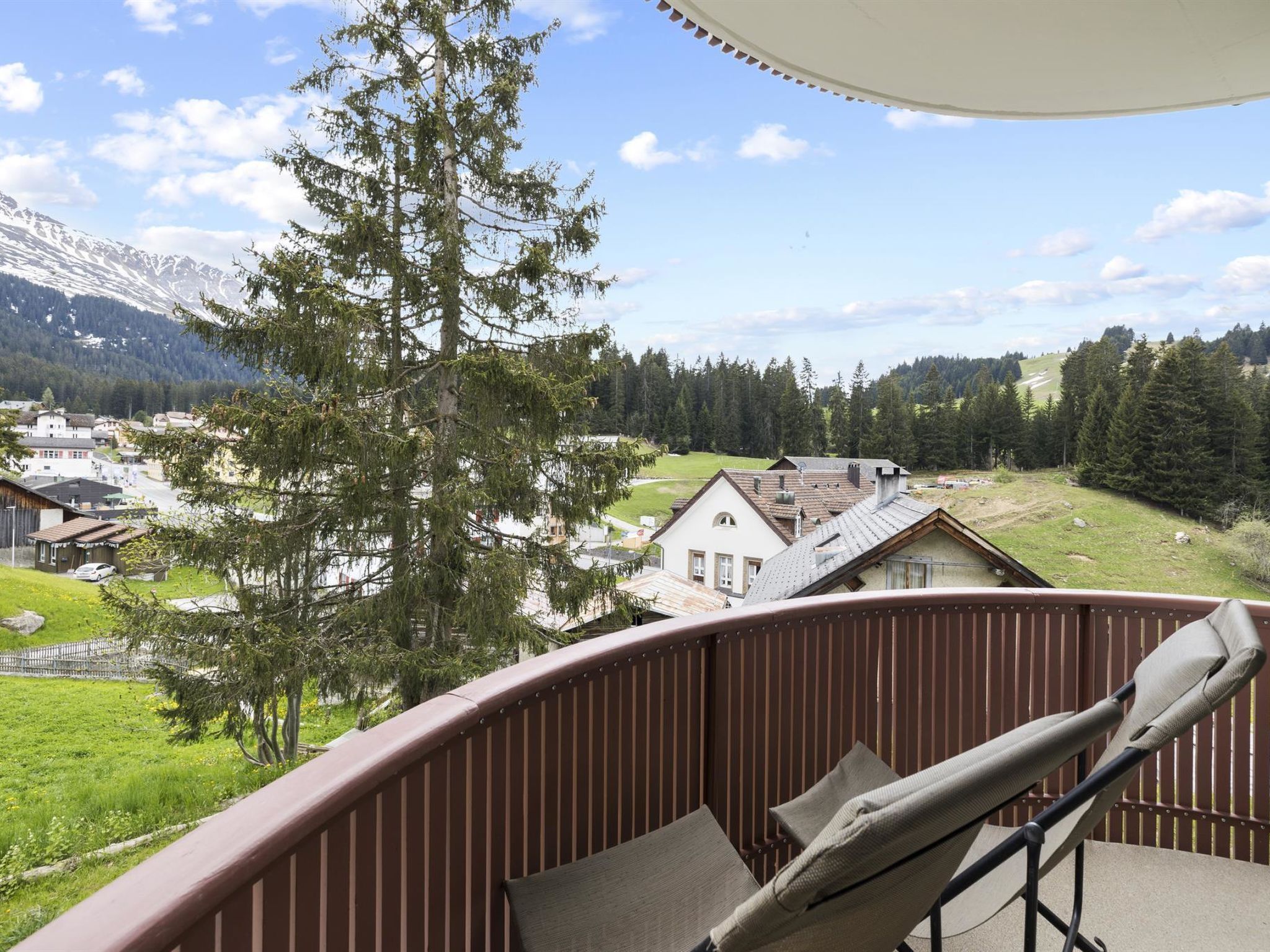 A balcony with a view of a village, a mountain, and a large tree.
