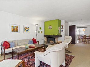 Uma sala de estar com sofá, poltrona, mesa de centro, lareira e obras de arte na parede.