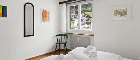 Une chambre d’hôtel avec deux lits, une chaise, une fenêtre donnant sur des maisons et des œuvres d’art accrochées aux murs.