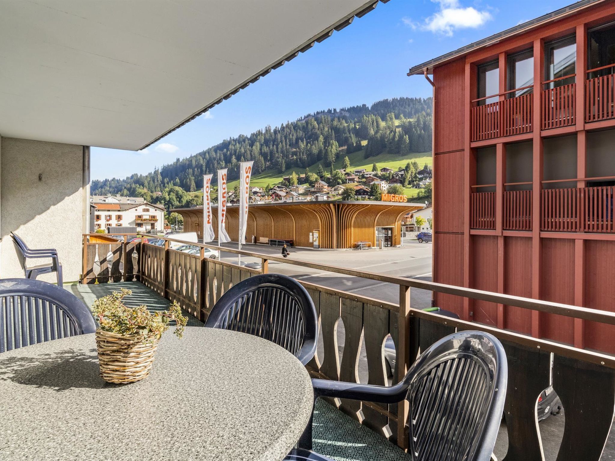 Un balcón con mesa y sillas, con vistas a un pueblo y colinas.