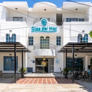 Un hotel llamado 'Olas del Mar' con fachada blanca, un balcón y una zona de estar exterior techada.