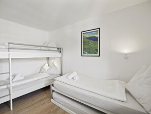 Une chambre avec un lit superposé, un lit simple et un tableau représentant un paysage, accroché au mur.