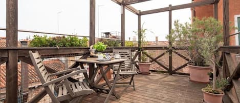 A wooden deck with a table and chairs, surrounded by potted plants.