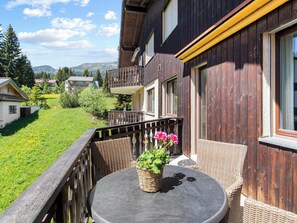 A balcony with wicker furniture, a table, and a potted plant with flowers. - A302 Appartement/Fewo A302 IH by Interhome (Lenzerheide)