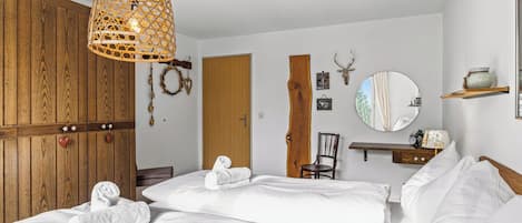 Une chambre d’hôtel avec une armoire en bois, un lit avec du linge de maison blanc, un luminaire suspendu et un miroir fixé au mur.