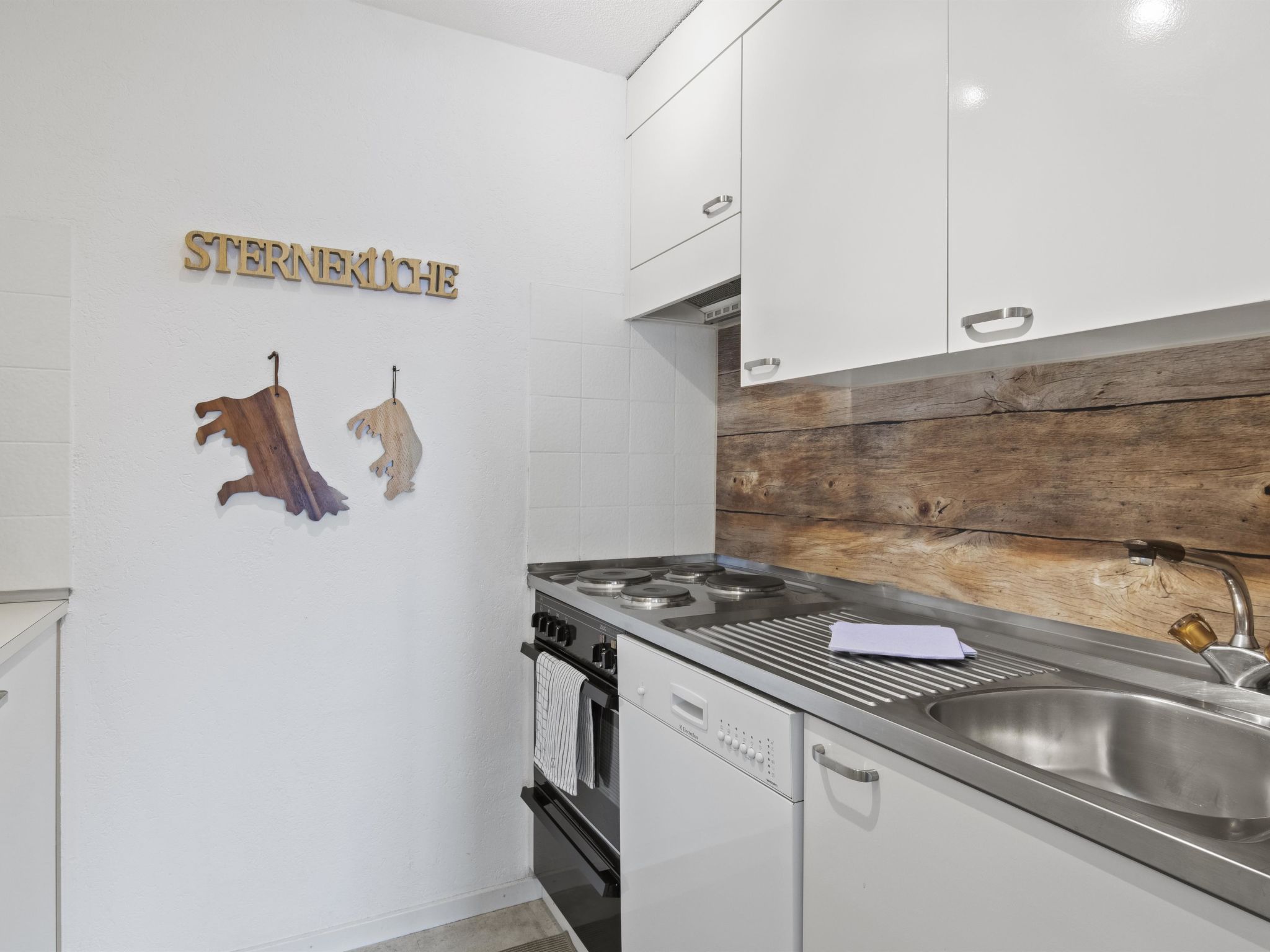 Eine Küche mit weißen Schränken, einer Spüle aus Edelstahl und Holzdekor an der Wand.