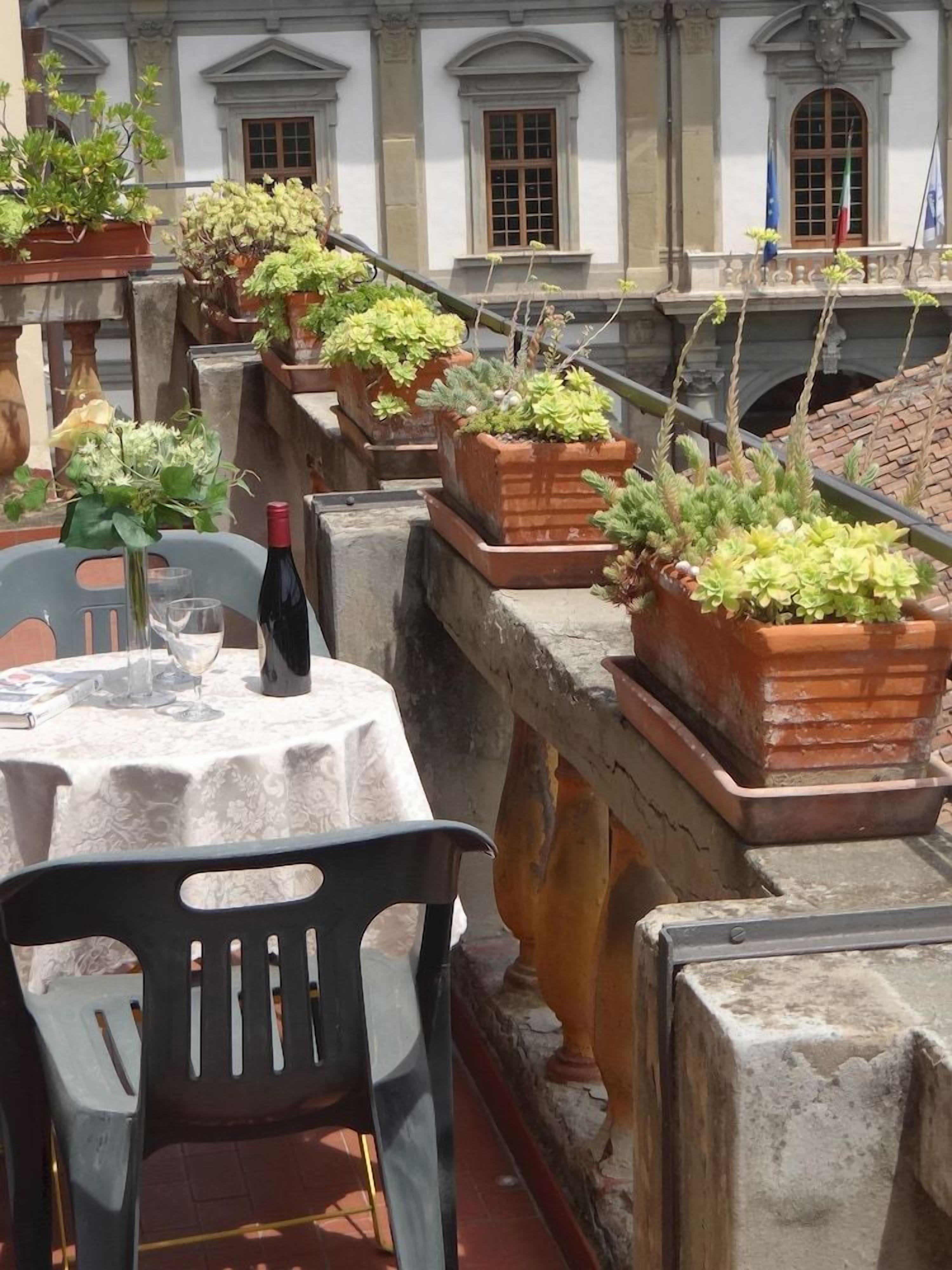 Una terrazza con piante in vaso, un tavolo con una bottiglia e delle sedie.