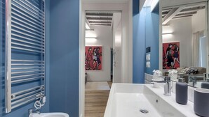 A bathroom with a white sink, a mirror, and a towel rack. There are two paintings on the wall.
