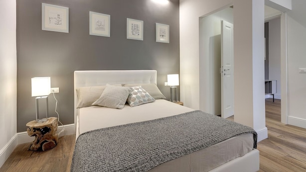 A bedroom with a bed, bedside lamps, a bedside table, and a wall-mounted light fixture.