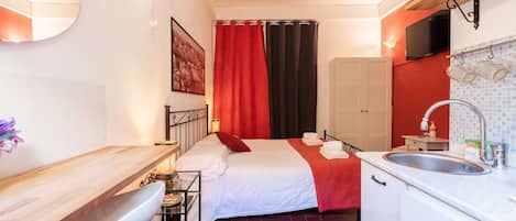 Una habitación pequeña con cama, una mesita, un lavamanos y un espejo.