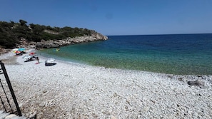 A pebble beach with clear water, a rocky shoreline, and a few umbrellas. - Lalloudes Seaside Accommodation (East Mani)
