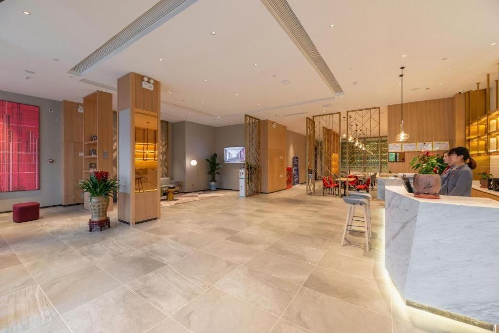 A modern hotel lobby with a reception desk, seating area, and a television screen.