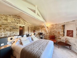 A bedroom with a stone wall, a bed with white bedding, a wooden chair, and a small table with a vase. - Hotel & Restaurant Des Basses Pyrenees (Bayonne)