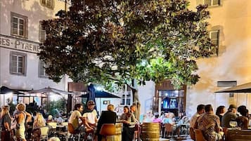 Un espace de café en plein air, avec des tables et des chaises, entouré de bâtiments portant des enseignes.