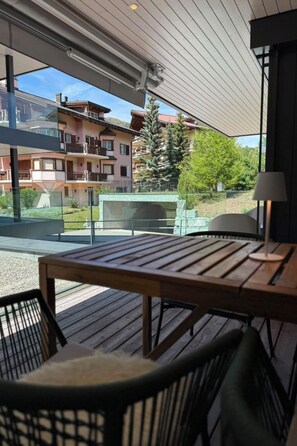 Eine Terrassengruppe im Freien mit Holztisch und -stühlen, einer Lampe und Blick auf ein Wohngebäude mit Balkonen.