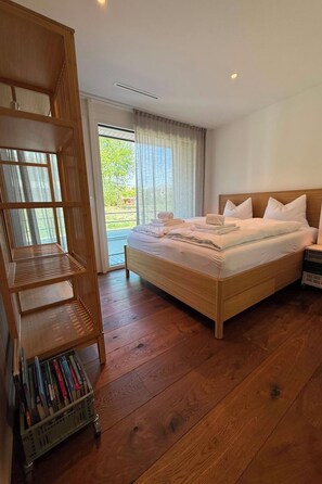 Hotellihuone, jossa on puinen sänky, puinen yöpöytä, sängyn vieressä oleva pöytä, puinen kirjahylly ja liukuovet, jotka johtavat ulkotilaan.