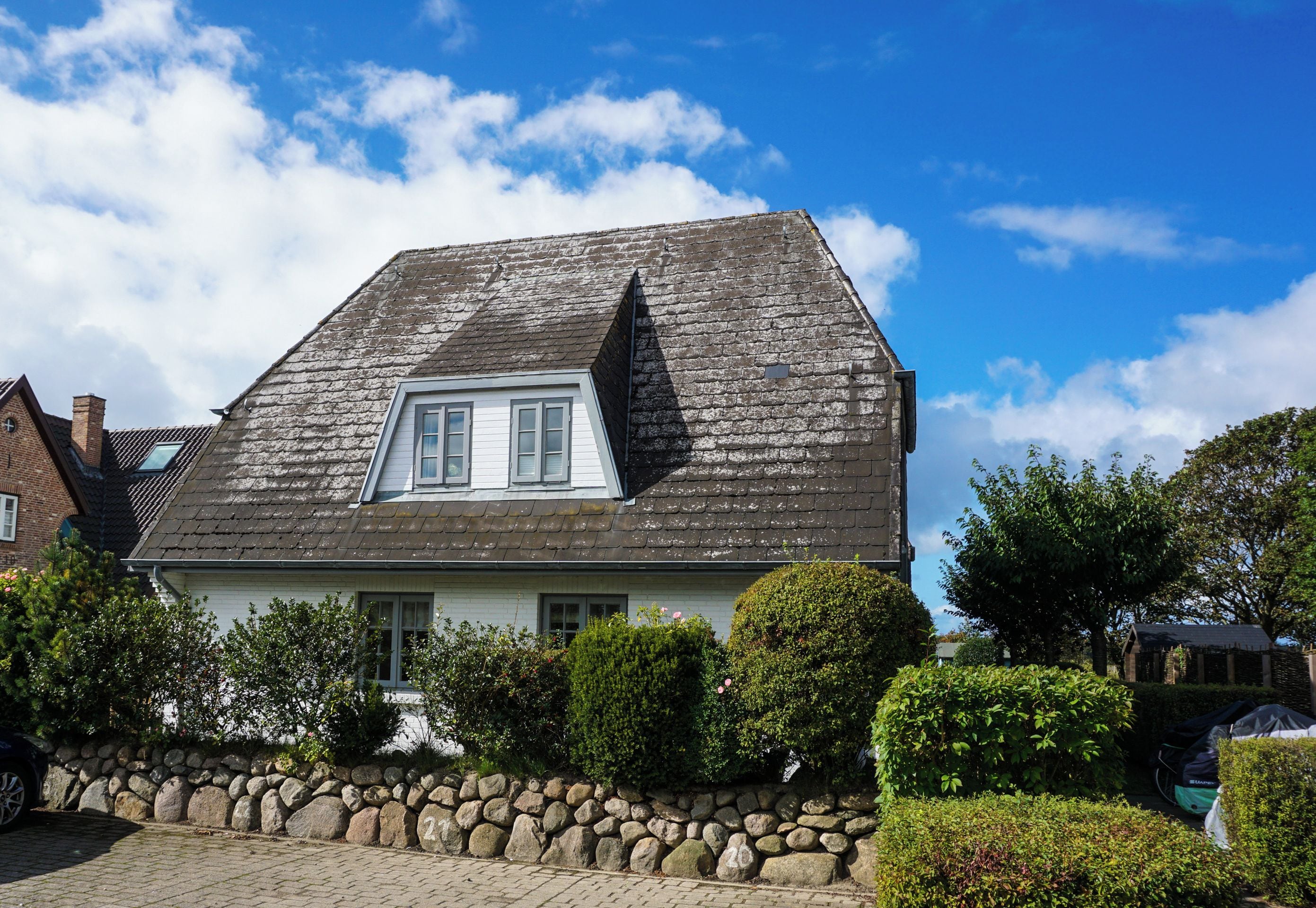 A house with a steeply pitched roof, a small attic window, and a stone wall in front.