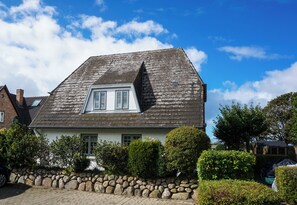 A house with a steeply pitched roof, a small attic window, and a stone wall in front. - Comfortable apartment in Keitum with a beach chair on Kampen Beach (Sylt)
