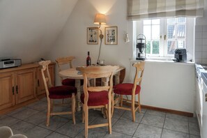 A cozy kitchen with wooden chairs, a table, a lamp, and a coffee machine. - Comfortable apartment in Keitum with a beach chair on Kampen Beach (Sylt)