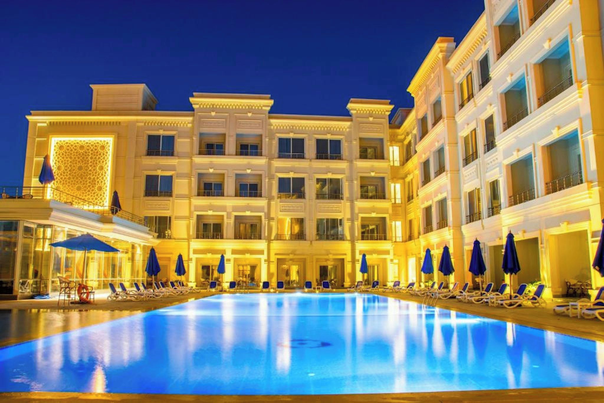 A hotel with a large indoor swimming pool, multiple balconies, and sun loungers.