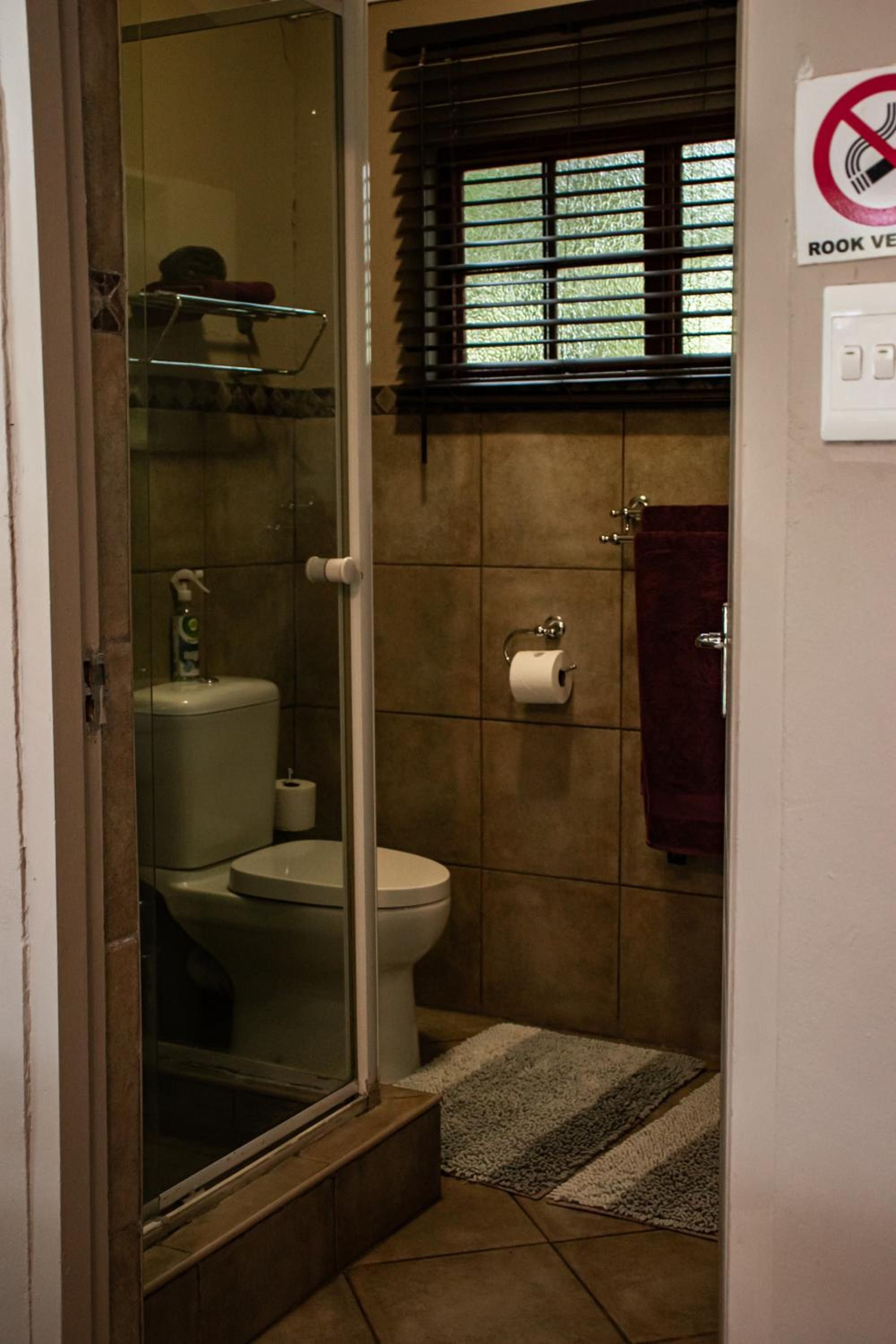 A bathroom with a glass shower enclosure, a toilet, a towel rack, and a window with blinds.