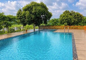 A rectangular swimming pool with a wooden deck surrounding it, trees in the background, and a clear sky.