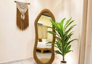 A room with a large mirror, a potted plant, and a bed with a white headboard.