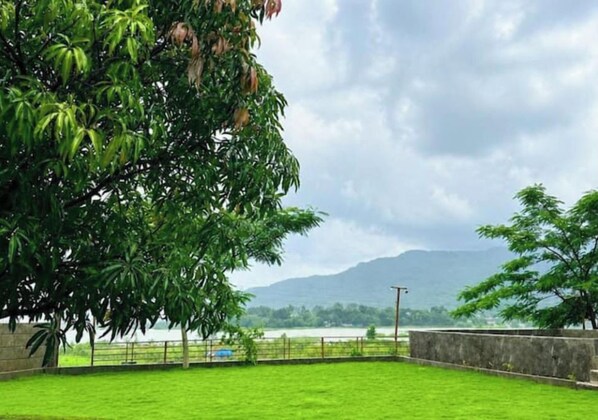A grassy area with a tree and a view of a body of water and mountains in the distance.